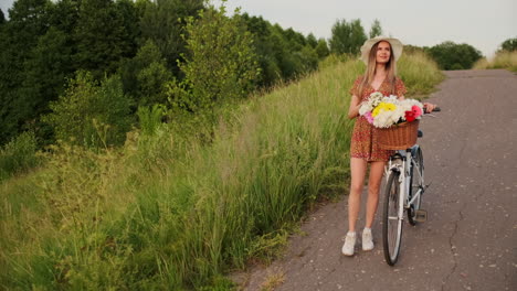 Slow-motion-sexy-beautiful-woman-with-a-bike-in-a-hat-and-a-light-summer-dress-comes-with-flowers-in-a-basket-and-smiles.